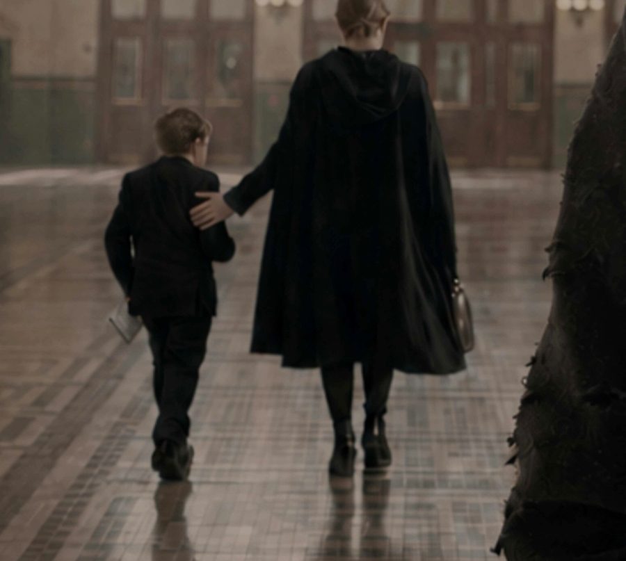A woman in a dark cloak and a young boy walk away across the station floor
