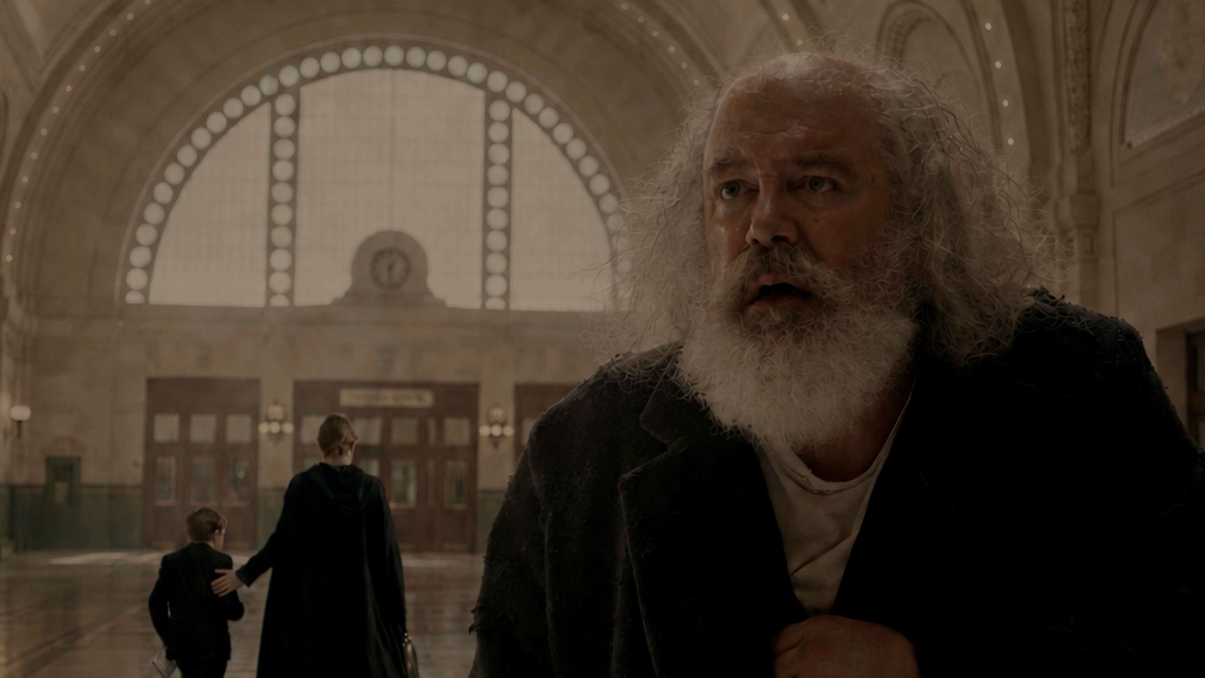 Arthur, an old man with a white beard, stands in the hall of Union Station while a woman and a boy walk away toward the doors.